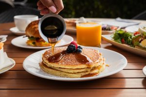 Pouring syrup over pancakes topped with fresh berries during breakfast at Catalina Kitchen, Terranea Resort in Rancho Palos Verdes.