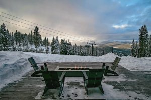 Snow-covered Northstar ski slopes with chair lifts ascending the mountain, skiers gliding down runs, and an outdoor fireplace terrace in the foreground, surrounded by tall pine trees.