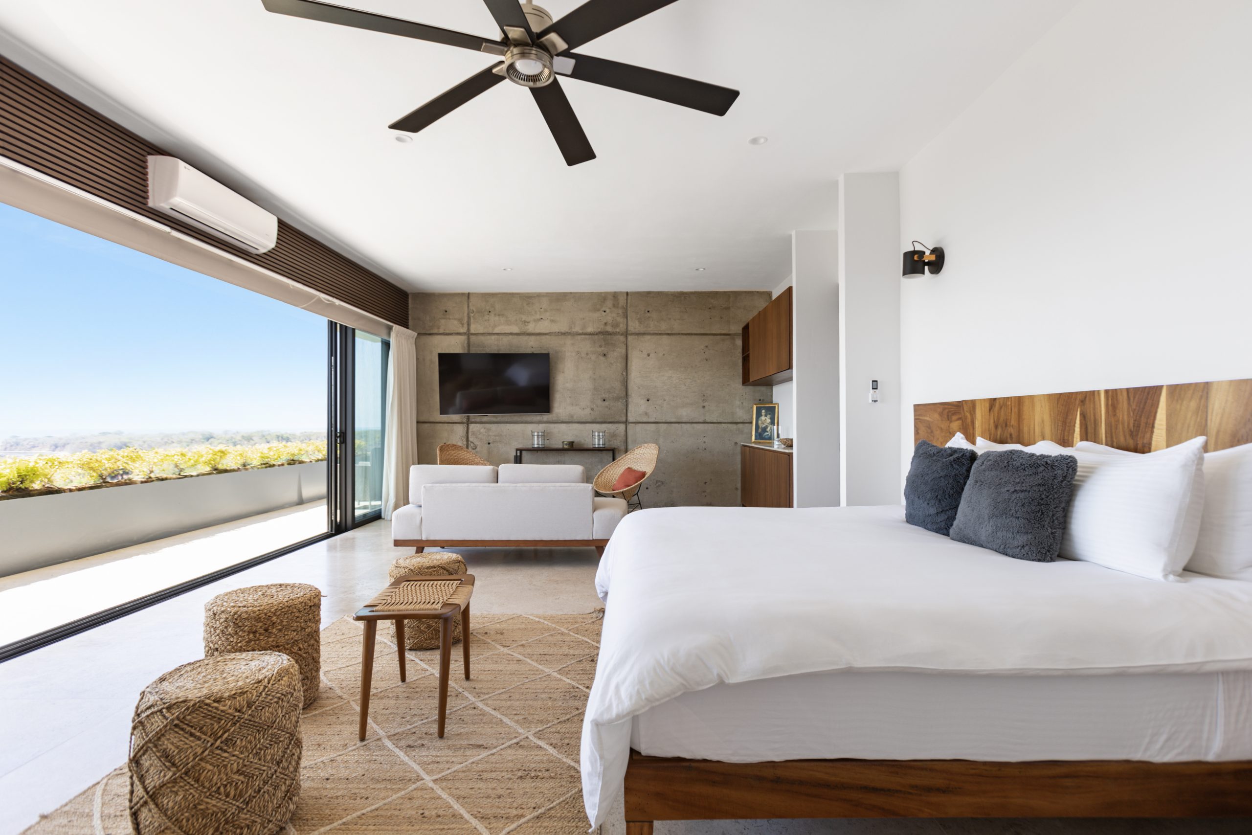 edroom with panoramic ocean views through large corner windows, light-colored curtains, and a cozy chair with a blanket.