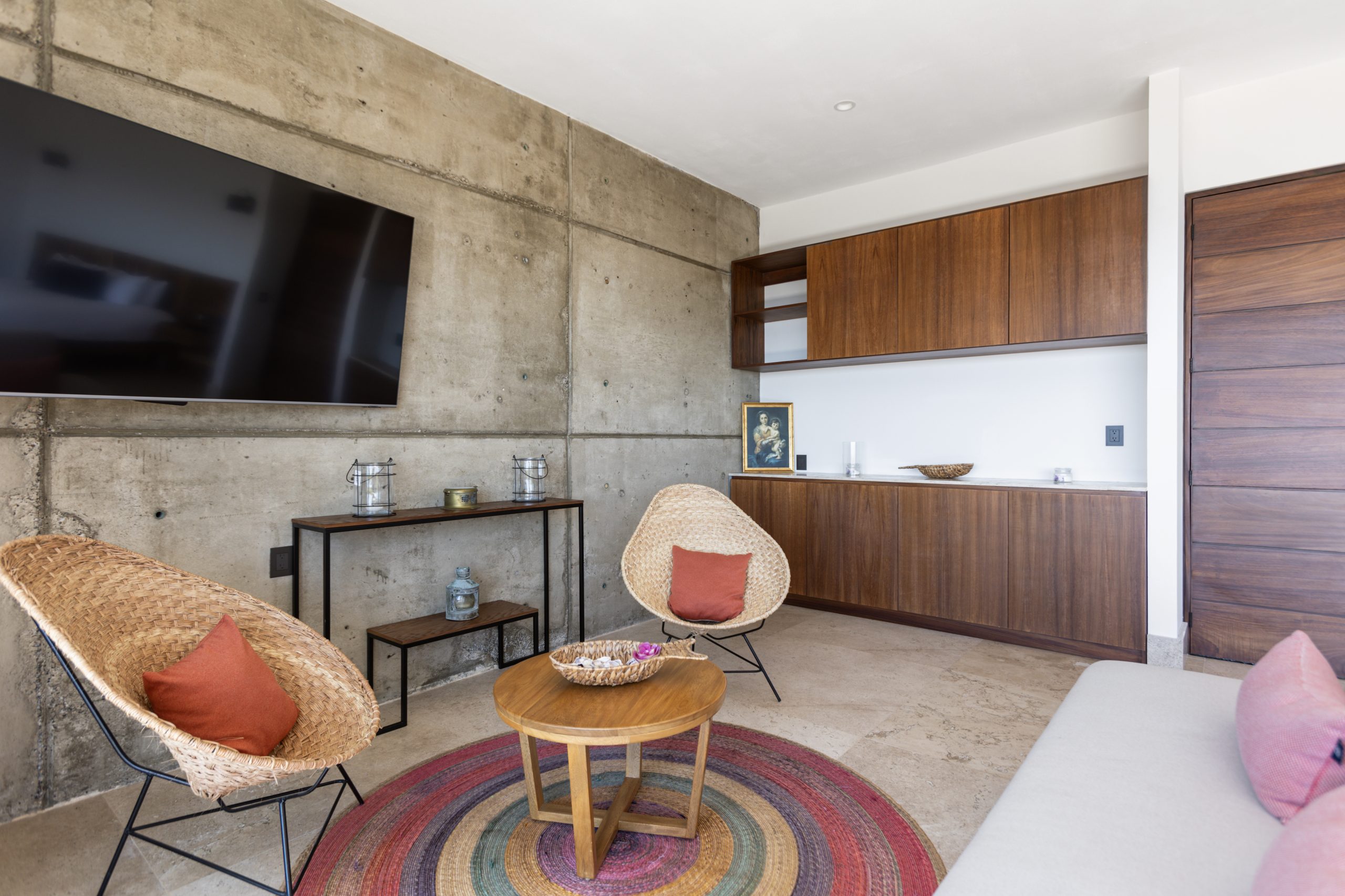 Modern living room with concrete accent wall, large TV, yellow sofa, gray armchairs, and glass doors opening to a pool view.