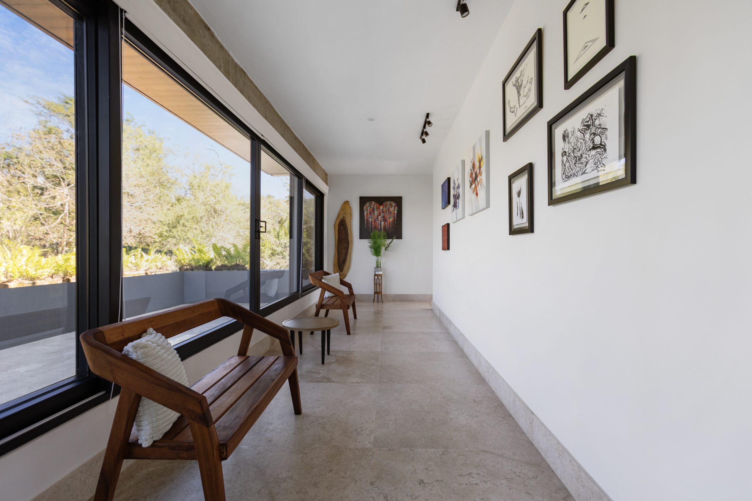 Bright hallway with large windows, wooden benches, and an art gallery wall displaying colorful framed paintings and prints