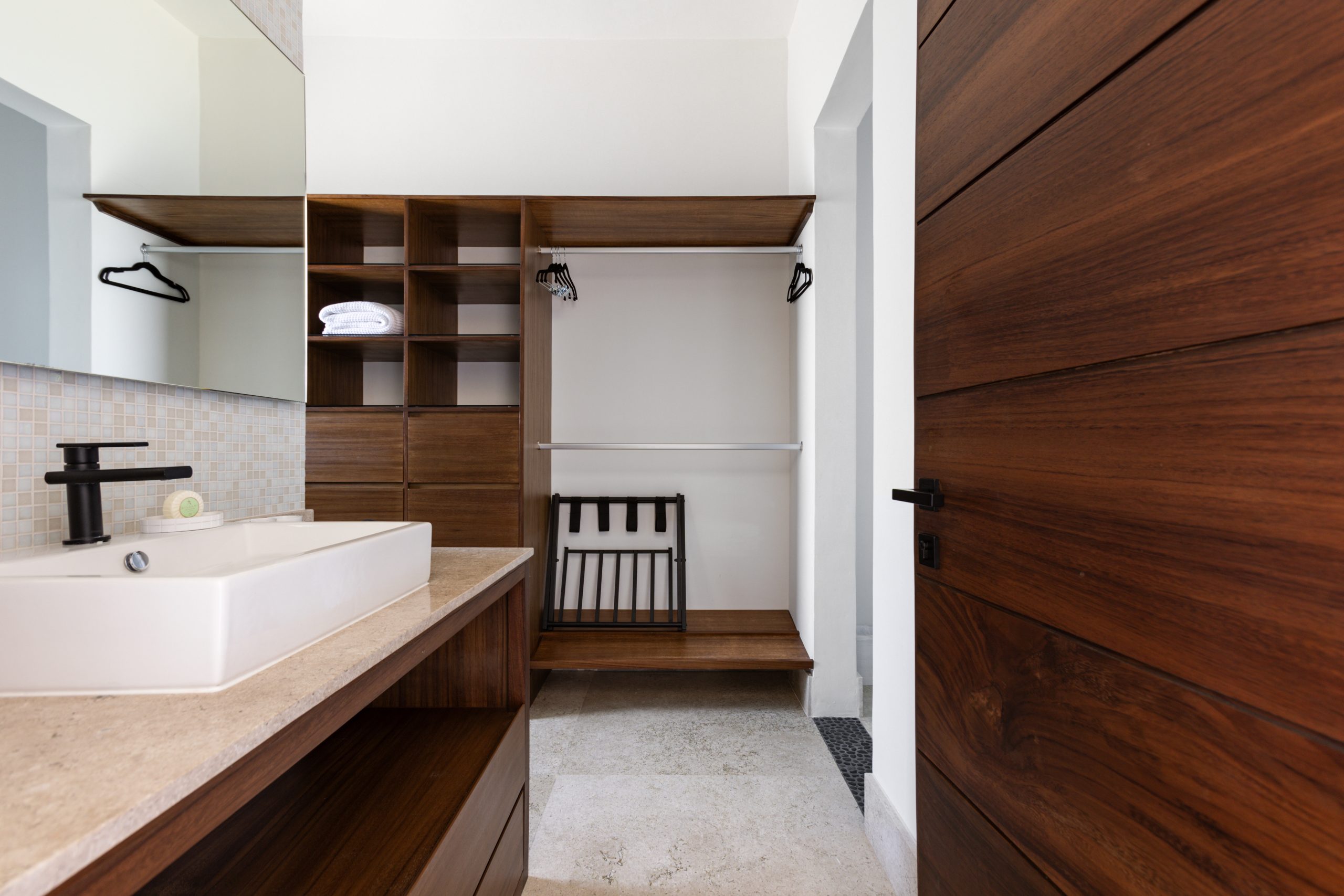 Contemporary bathroom with glass-enclosed shower, large mirror, wooden vanity, and built-in closet with open shelving and drawers