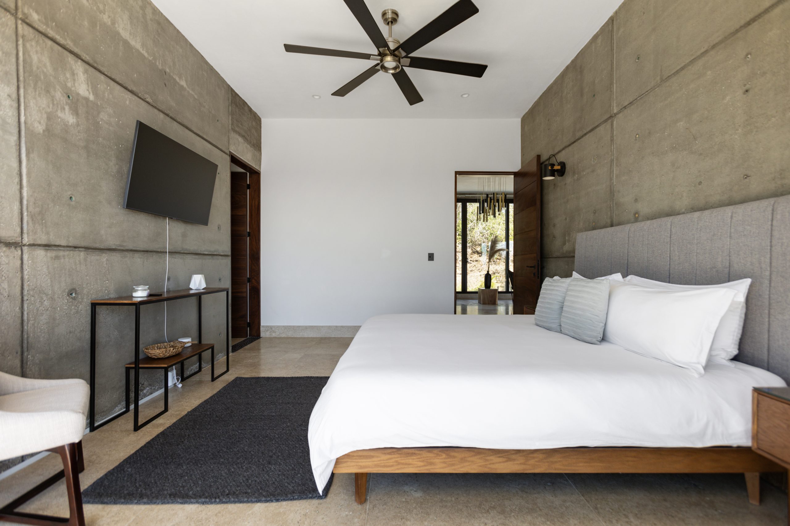 edroom with panoramic ocean views through large corner windows, light-colored curtains, and a cozy chair with a blanket.