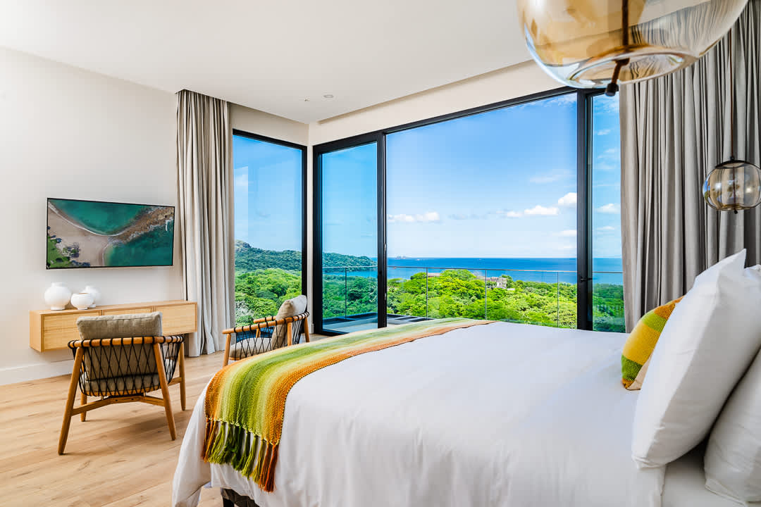 Luxury bedroom with floor-to-ceiling windows overlooking lush greenery and ocean views at the Reserva Conchal penthouse in Costa Rica