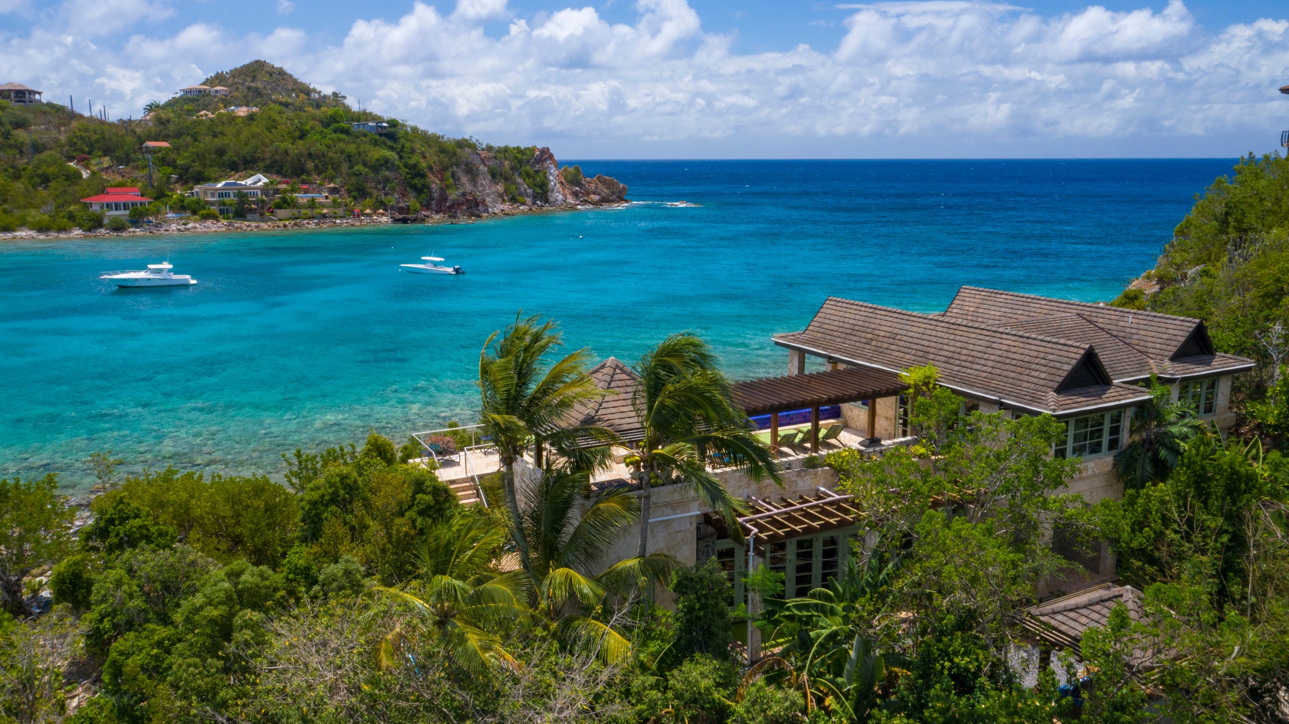 Luxury villa in St. John overlooking turquoise Caribbean waters with boats and palm trees.