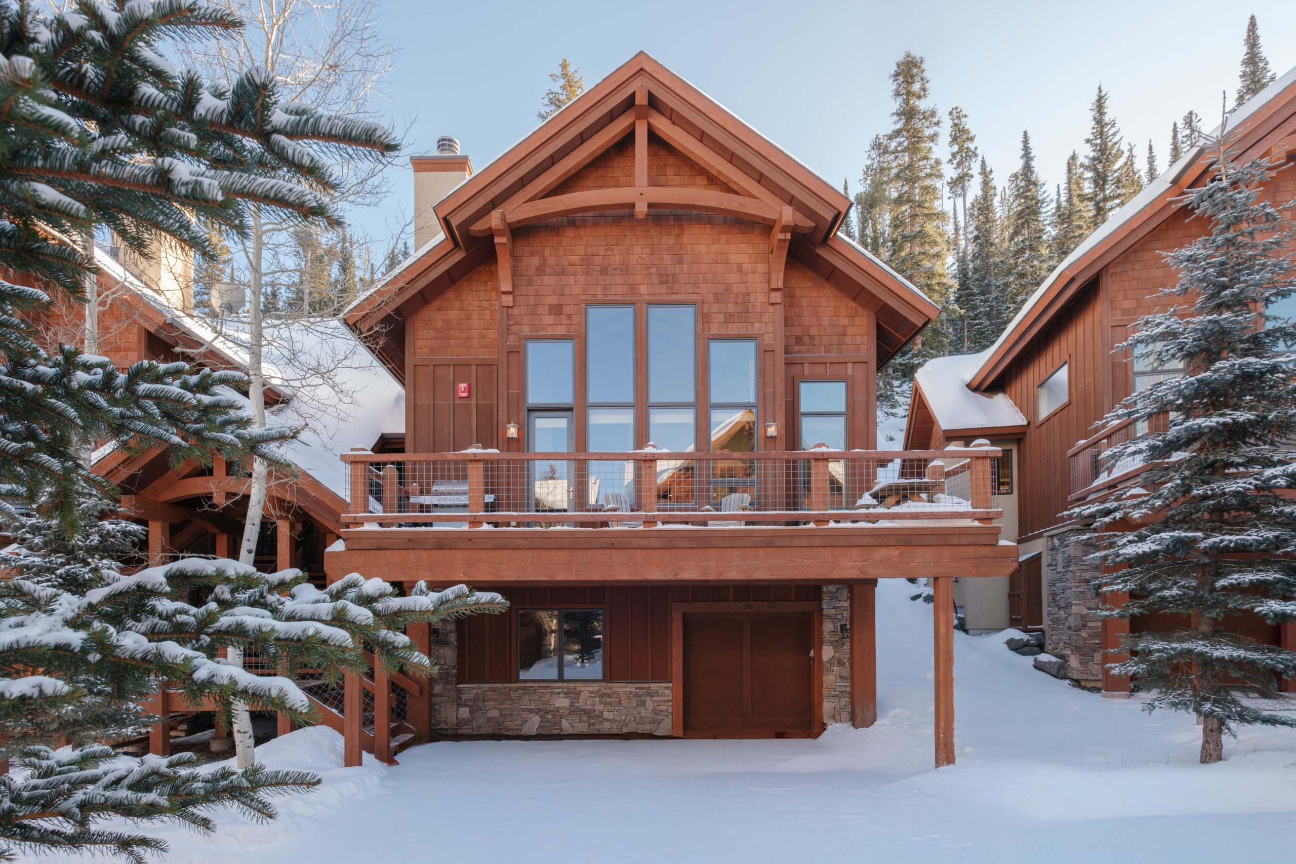 Stunning luxury home at Big Sky Resort surrounded by snow-covered mountains and tall pine trees.