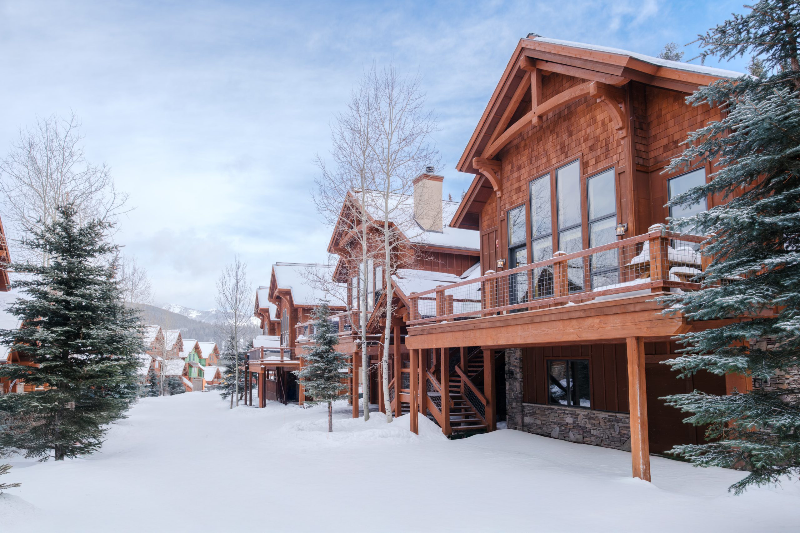 Stunning luxury home at Big Sky Resort surrounded by snow-covered mountains and tall pine trees.