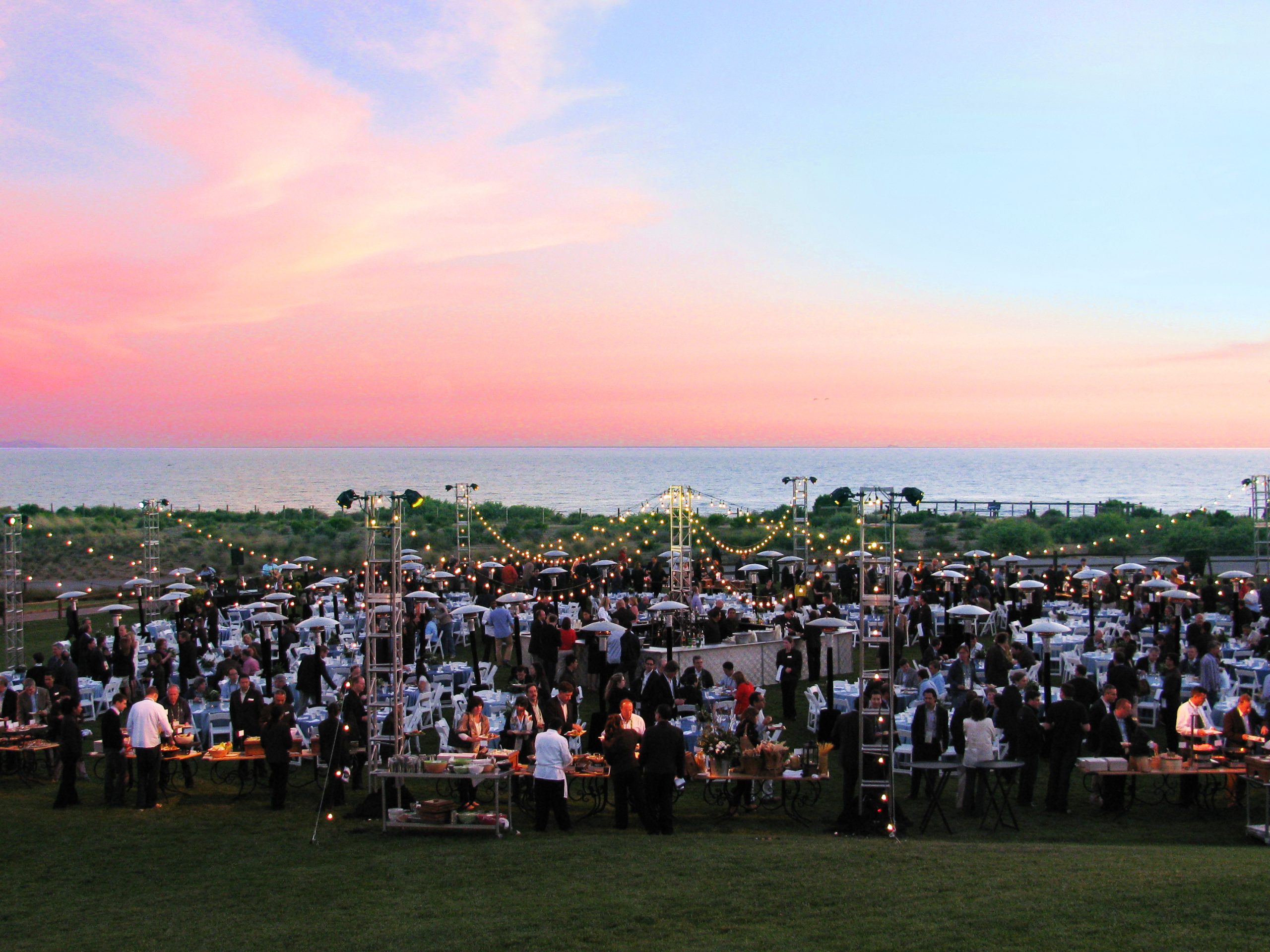 Elegant outdoor event at Terranea Resort featuring guests dining under string lights at sunset with panoramic ocean views along the California coast.
