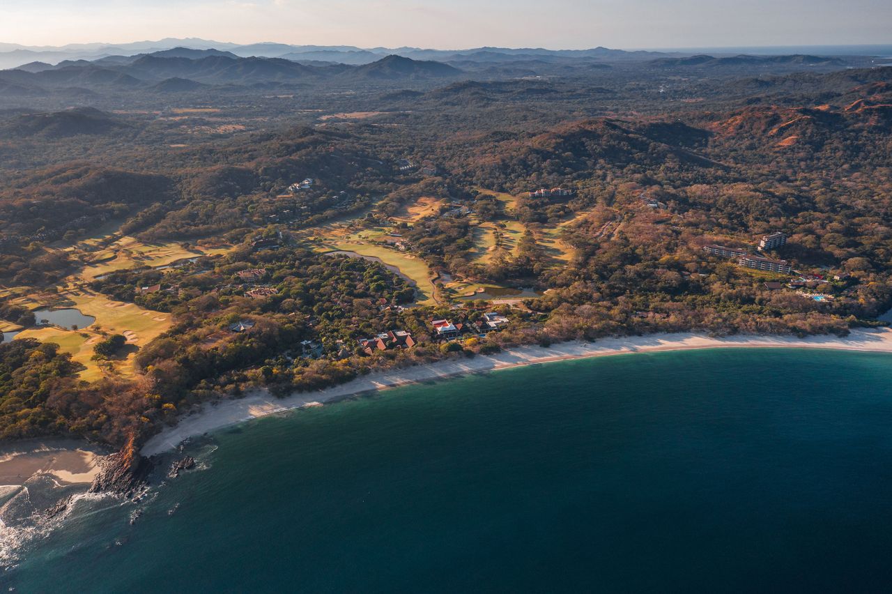 Aerial view of lagoon-style pool surrounded by palm trees and resort villas at the Westin Reserva Conchal.