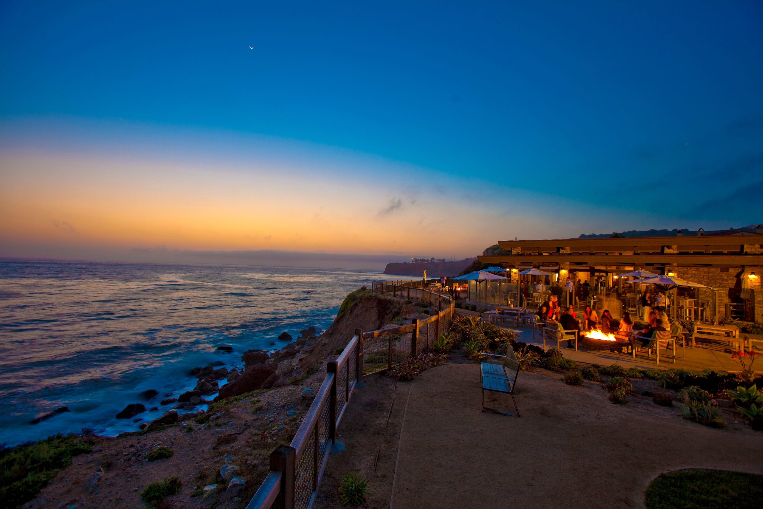 Cliffside dining at Nelson’s, Terranea Resort in Rancho Palos Verdes, with guests enjoying dinner by the fire pits overlooking the Pacific Ocean at sunset.