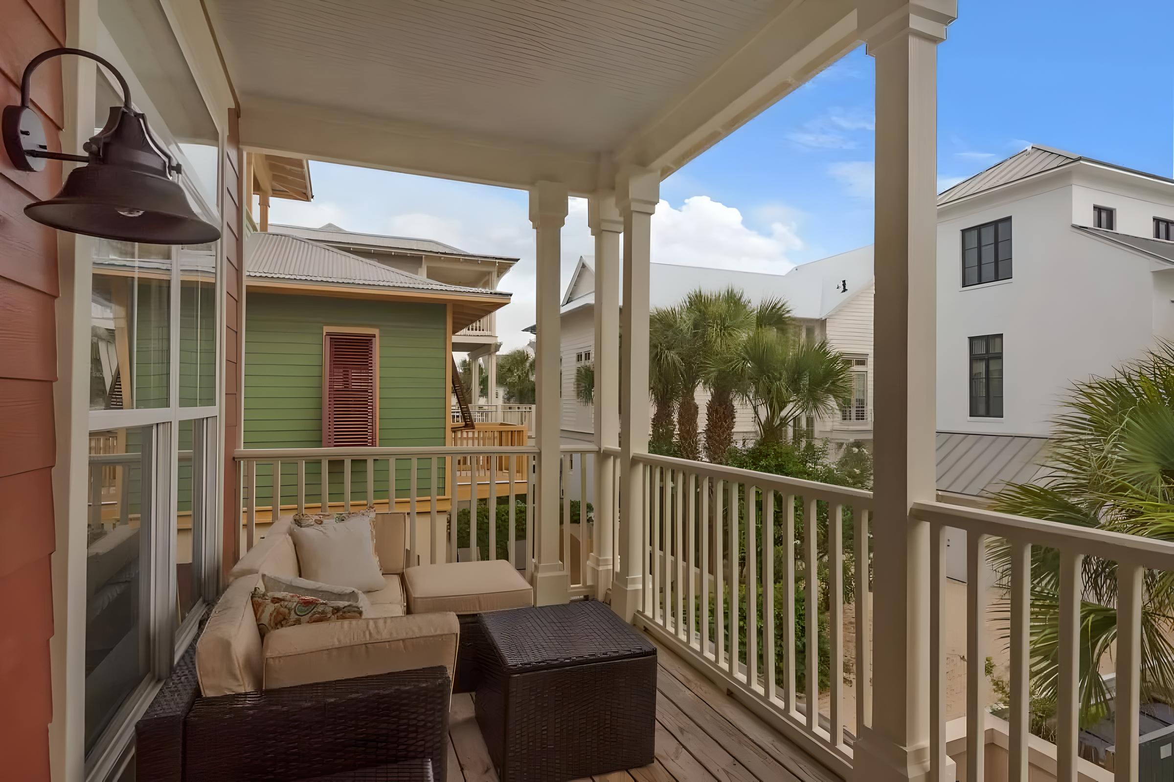 Balcony view of a luxury Seacrest Beach home featuring comfortable seating, palm trees, and neighboring coastal architecture, emphasizing proximity to the beach and ideal for family vacations or romantic getaways.