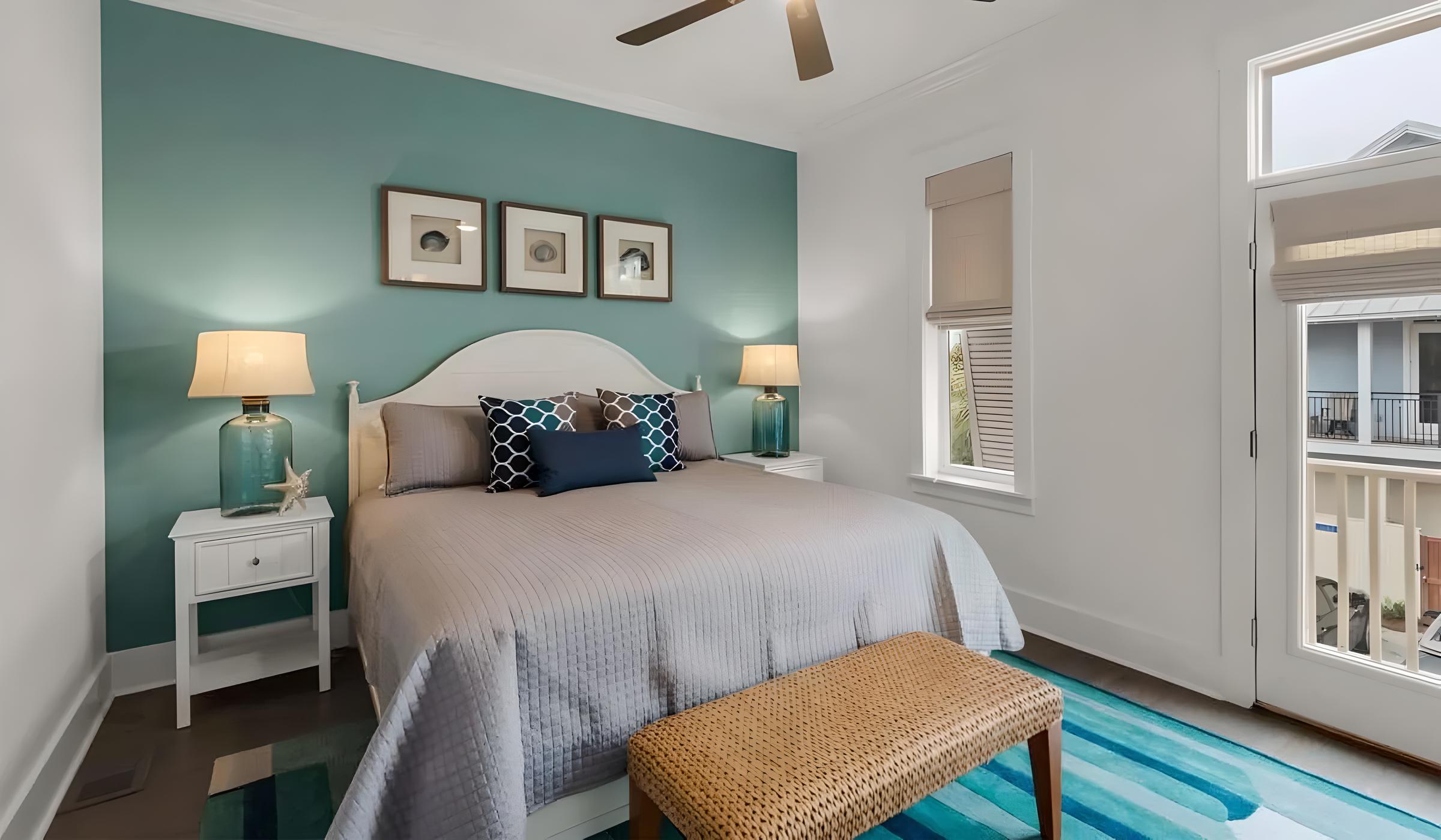 Luxury bedroom in Seacrest Beach home featuring teal accent wall, modern decor, comfortable bedding, stylish lamps, and a view of the outdoors.