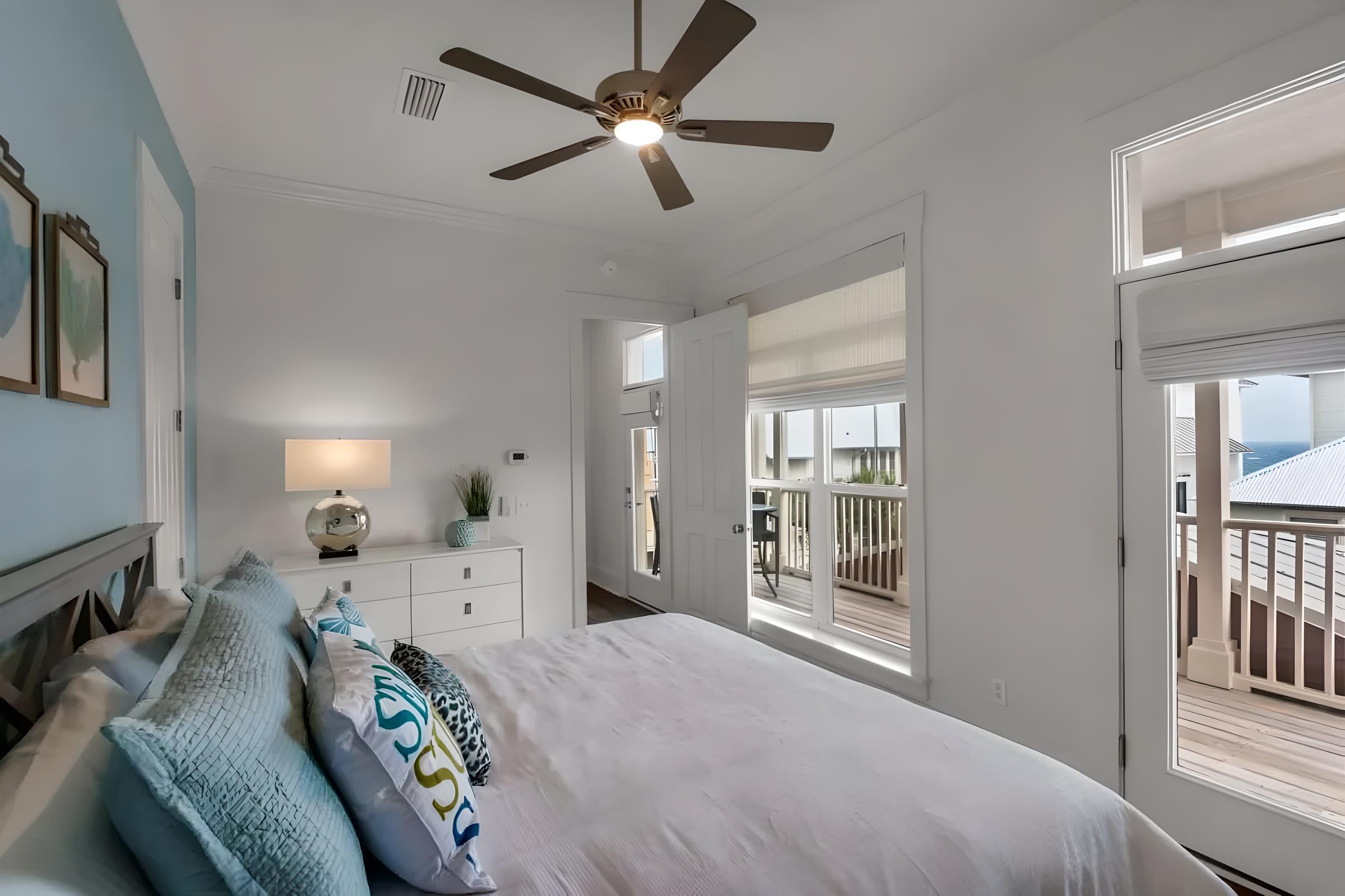 Luxury bedroom in Seacrest Beach home with blue accents, plush pillows, and balcony access overlooking the Gulf of Mexico, showcasing modern design and comfort for family vacations or romantic getaways.