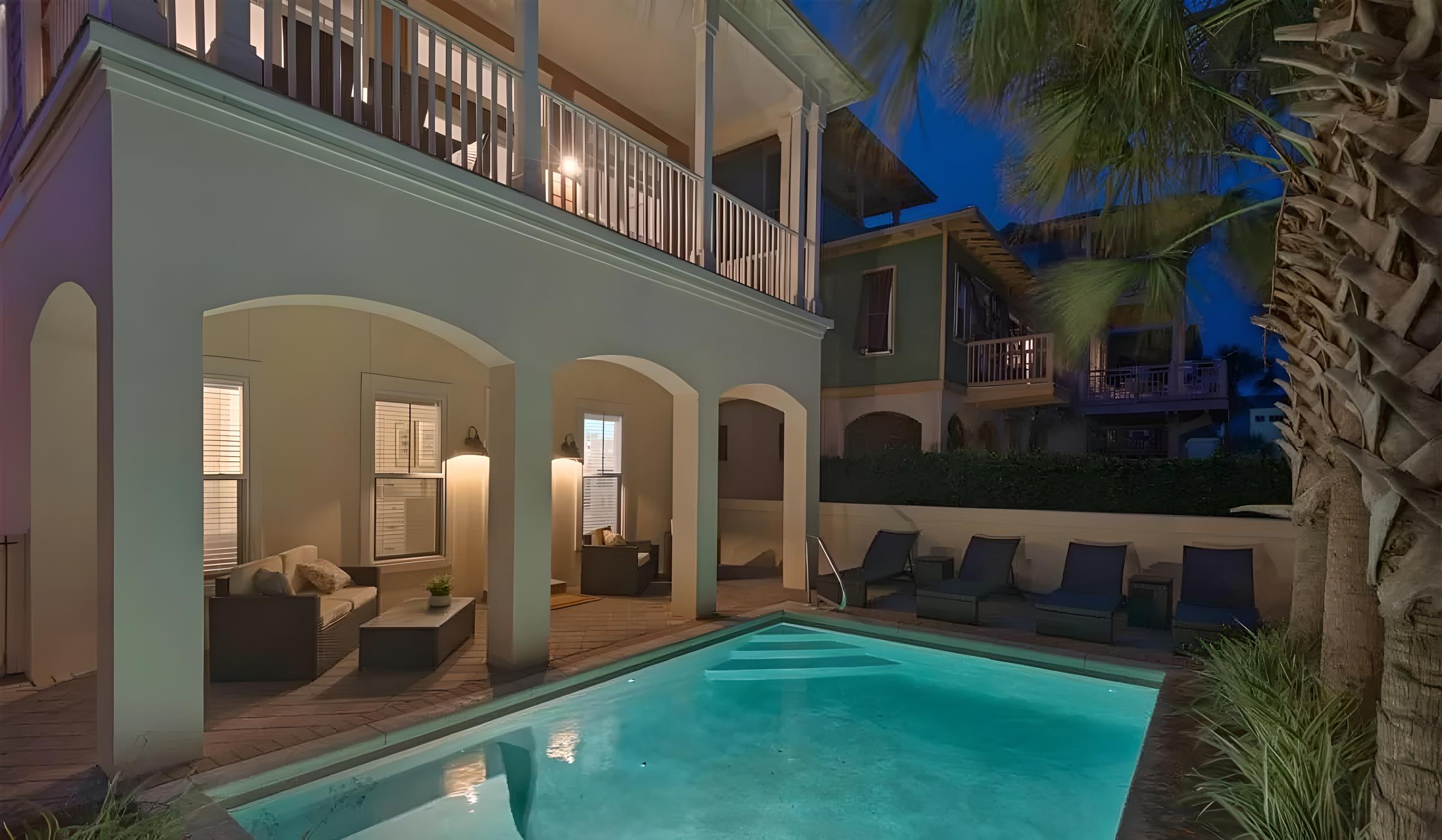 Luxury Seacrest Beach home with illuminated pool area, outdoor seating, and palm trees, showcasing modern design and inviting ambiance for family vacations or romantic getaways.