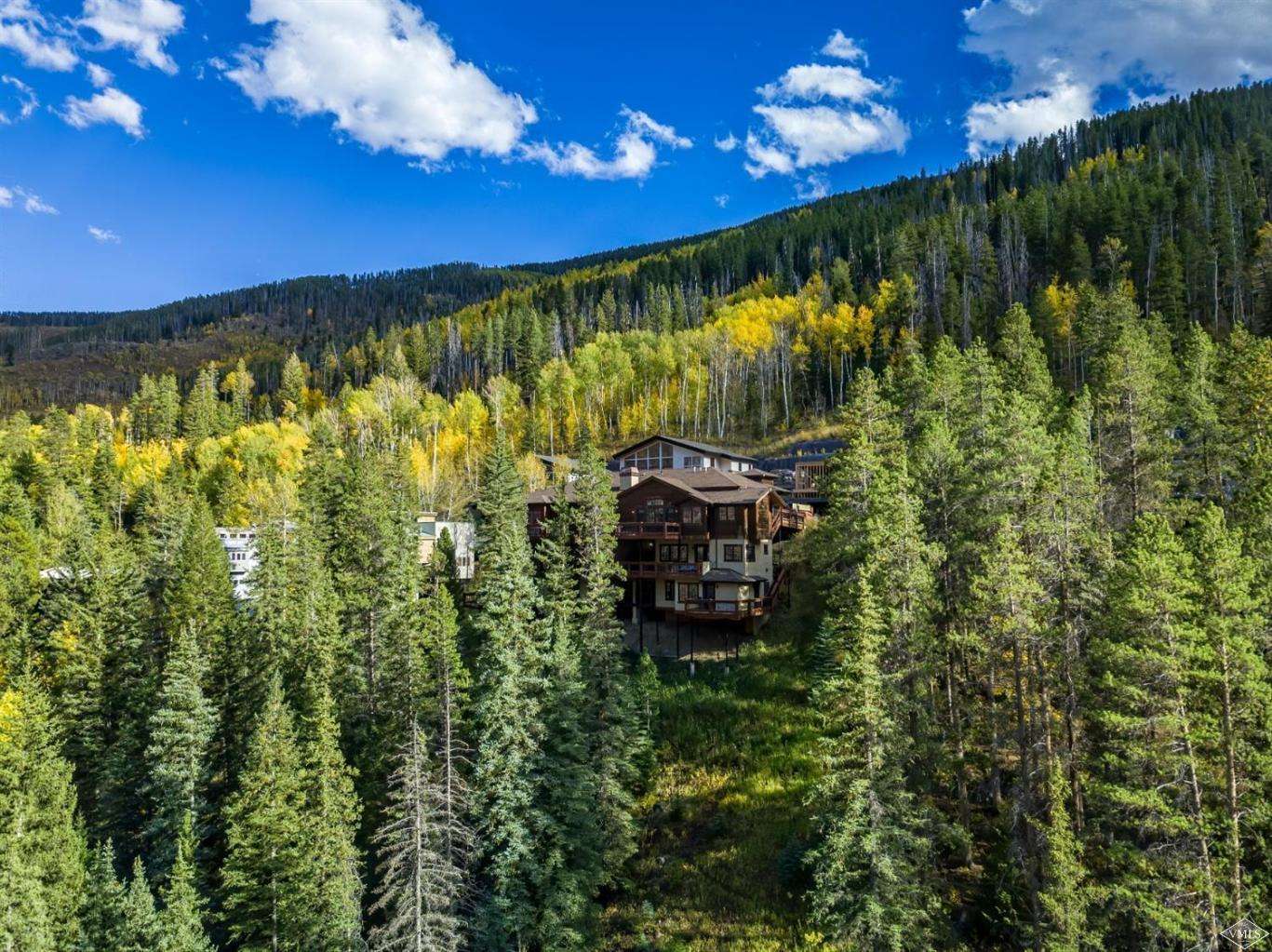 Vail, Colorado alpine landscape featuring snow-dusted mountains and pine trees, with sunlight illuminating the slopes and charming mountain chalets in the valley below.