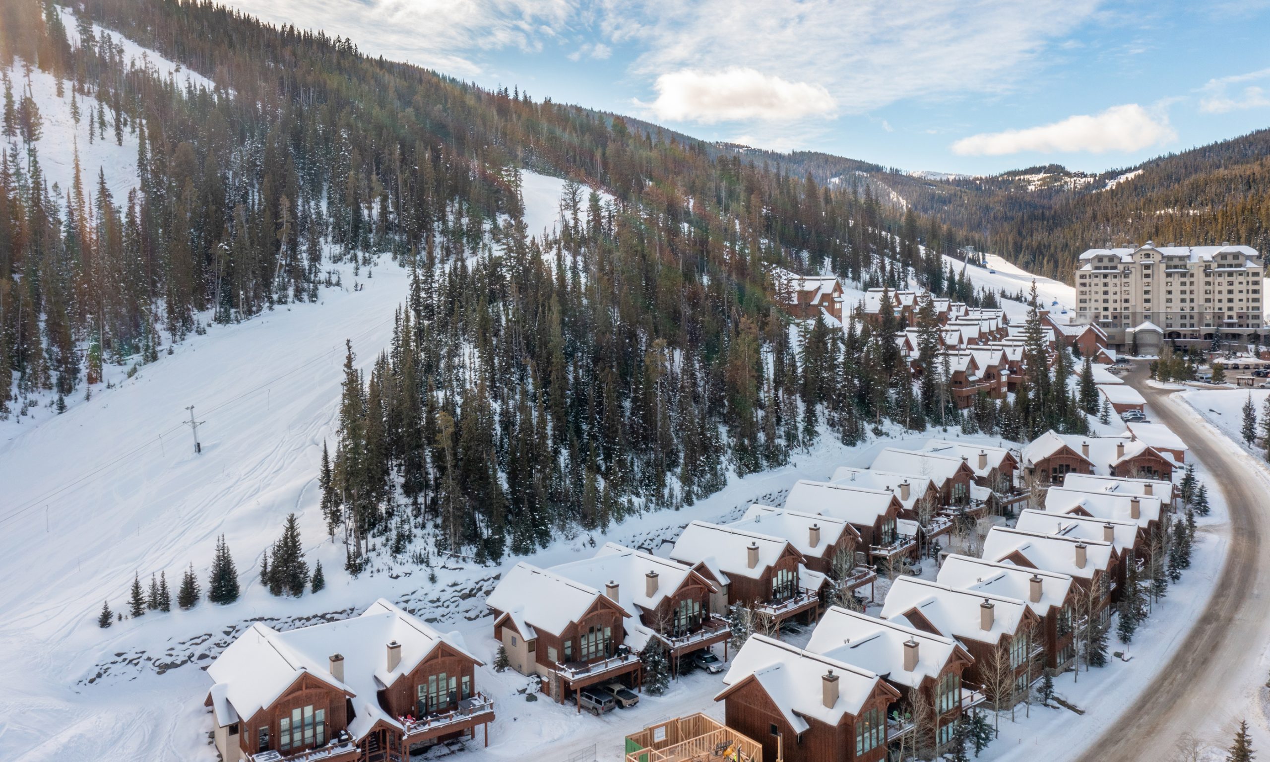 A scenic view of Big Sky Resort with snow-covered ski slopes rising behind a cluster of mountain lodges and homes in Montana