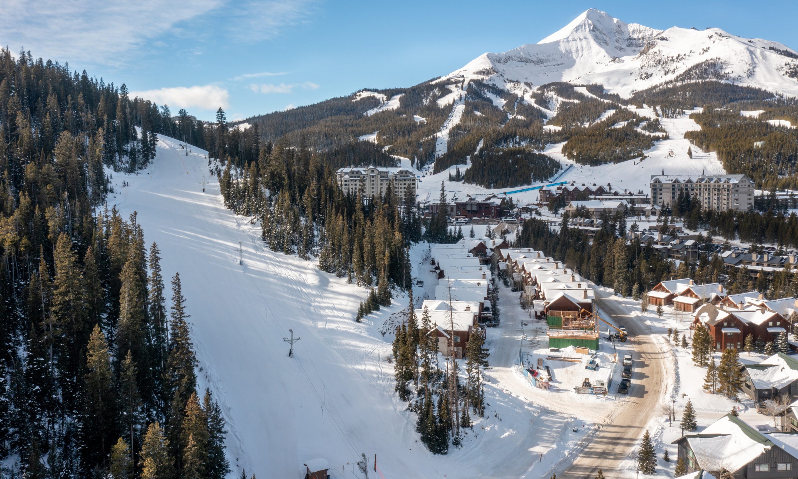 A scenic view of Big Sky Resort with snow-covered ski slopes rising behind a cluster of mountain lodges and homes
