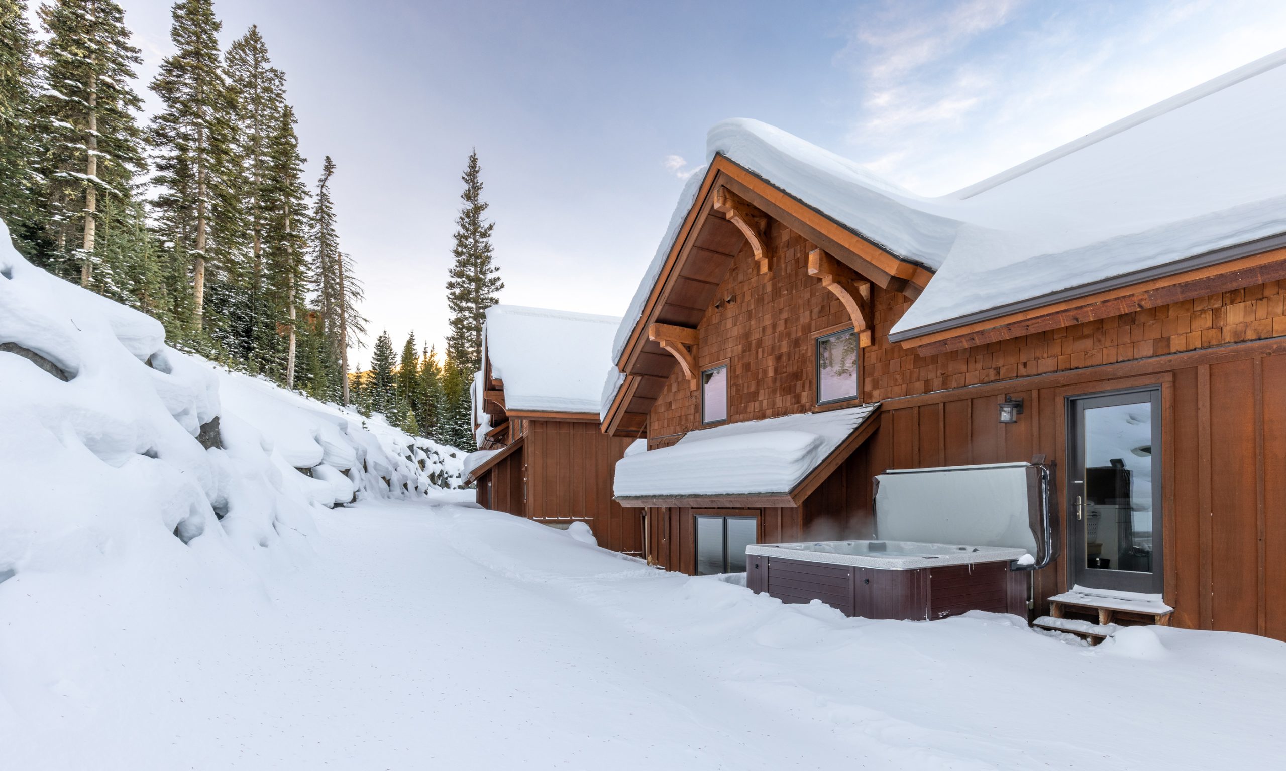 Luxury lodge in Big Sky, Montana with outdoor hot tub, snow-covered landscape, and panoramic views of surrounding trees and mountains.
