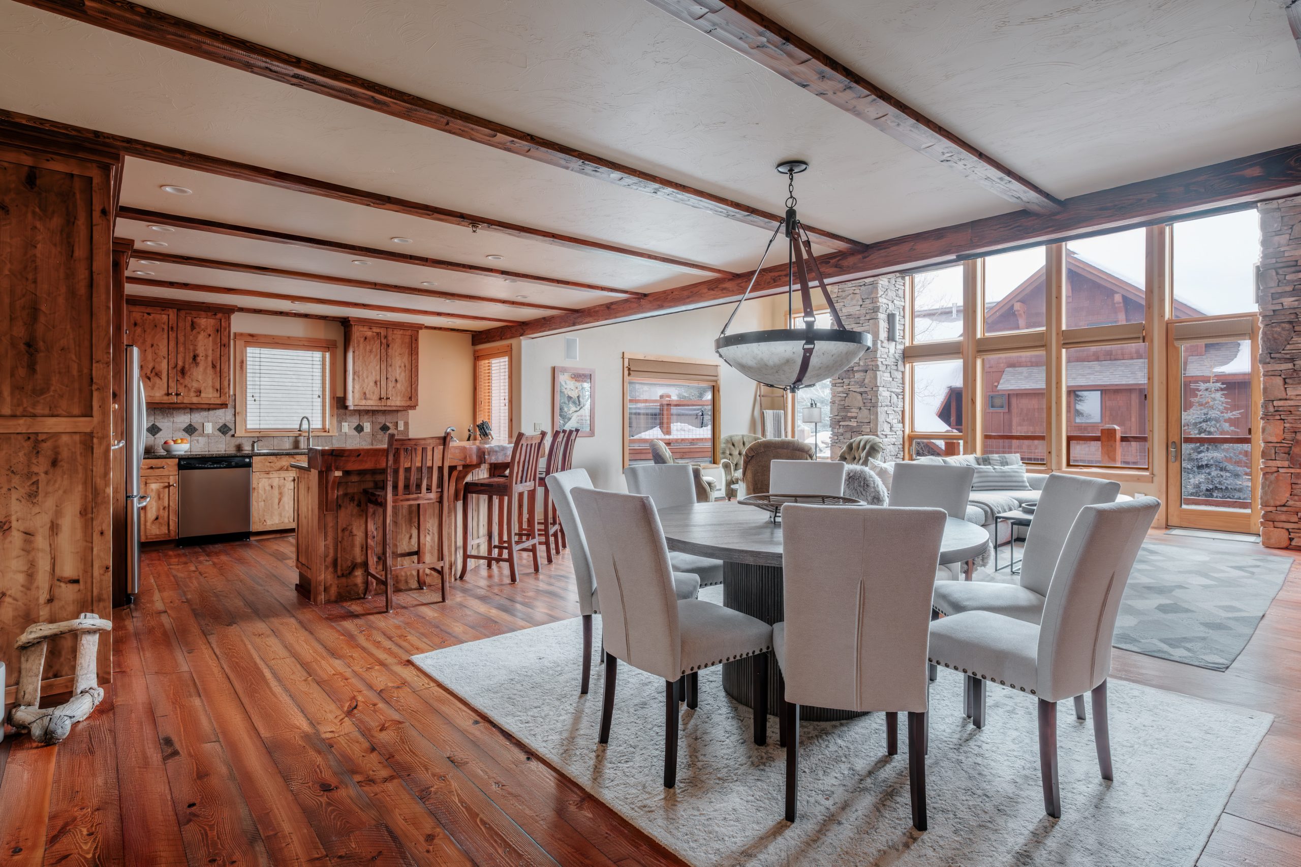Open-concept Big Sky resort great room with dining area, rustic wood beams, stone accents, and mountain lodge design