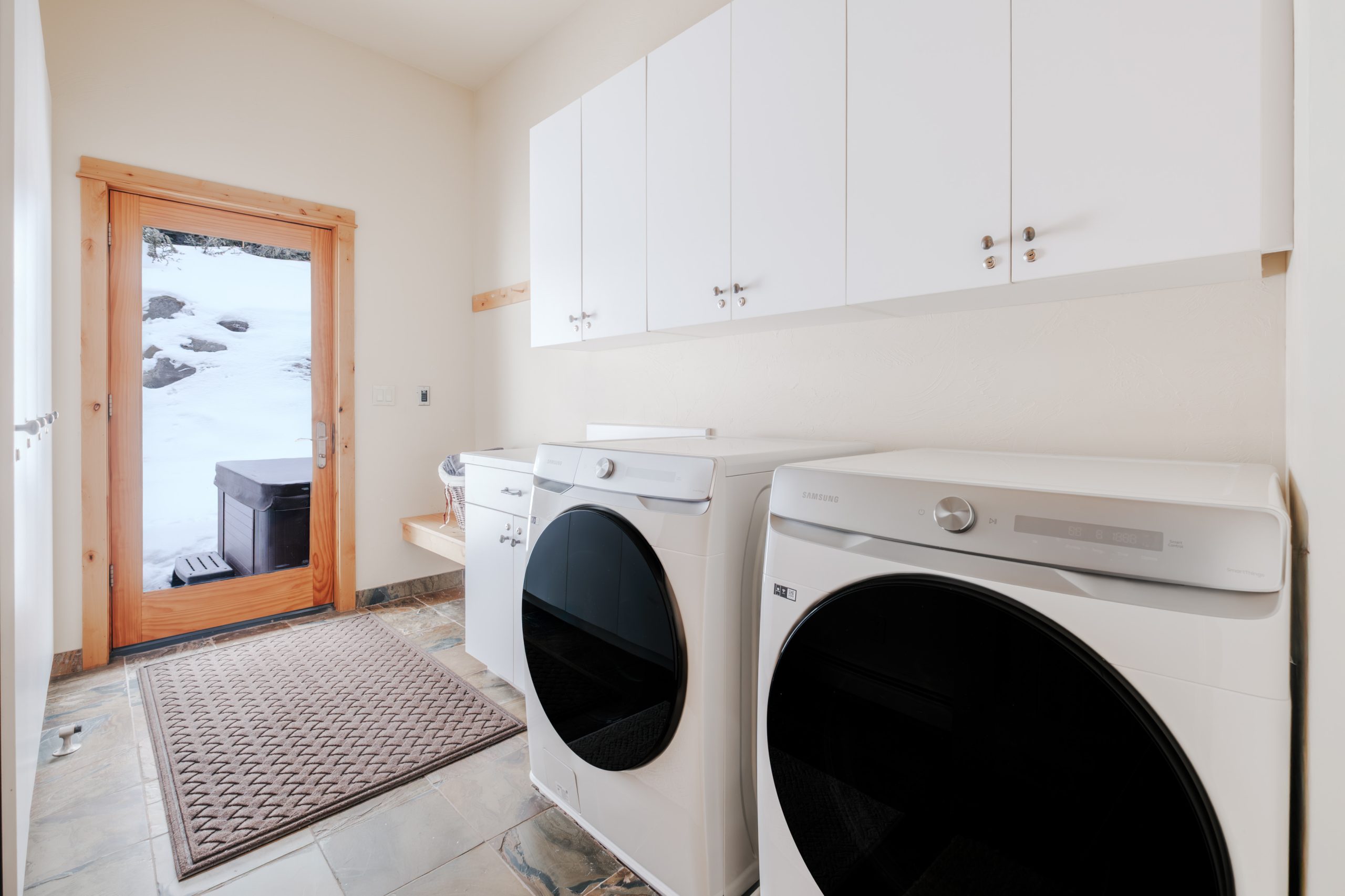 Luxury Big Sky resort laundry room with full-size washer and dryer, custom white cabinetry, and convenient outdoor access