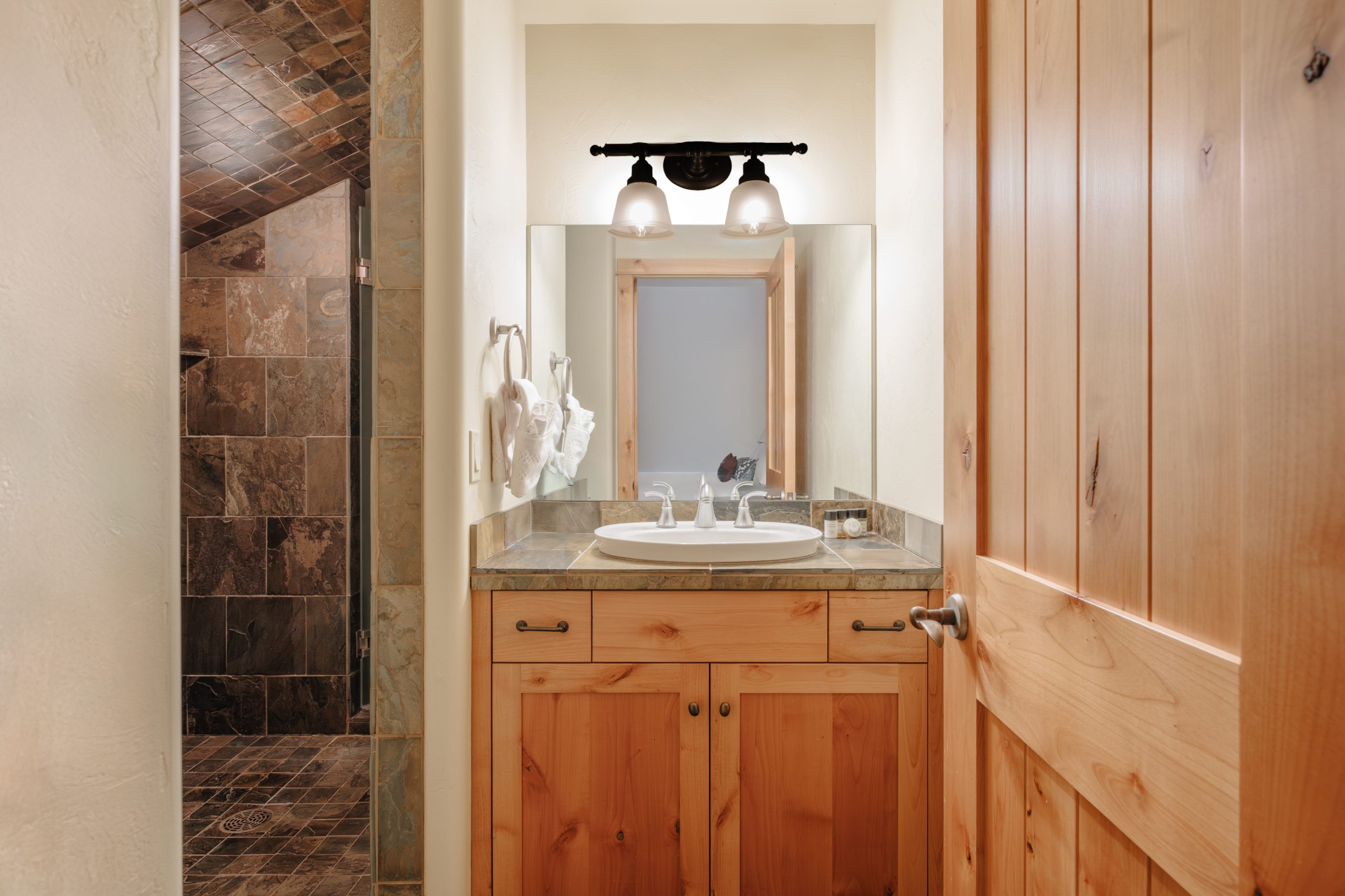 Big Sky resort bathroom with wood vanity, stone countertop, modern sink, and walk-in tiled shower