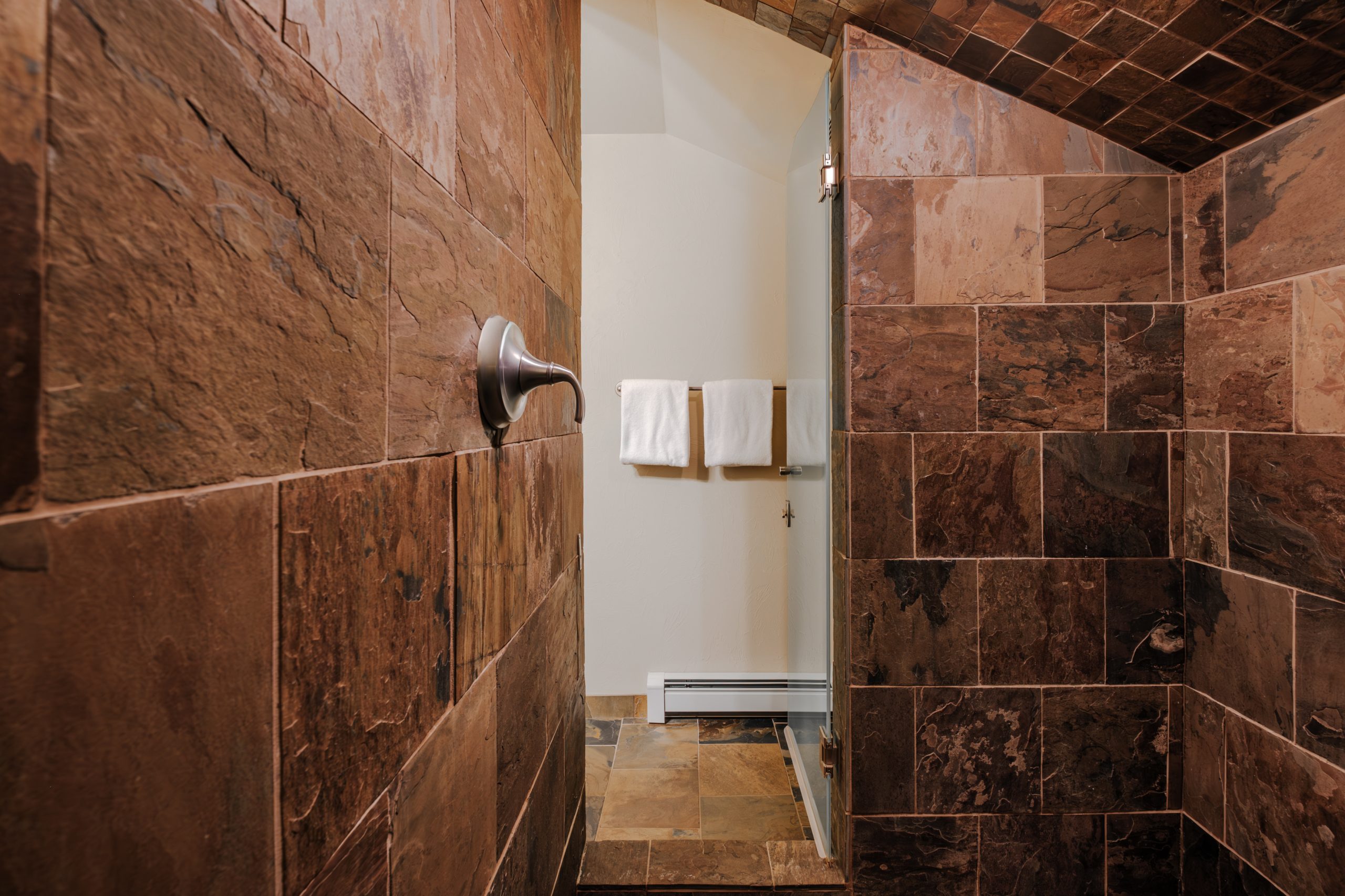Stone tile walk-in shower in Big Sky resort bathroom with rustic mountain lodge finishes
