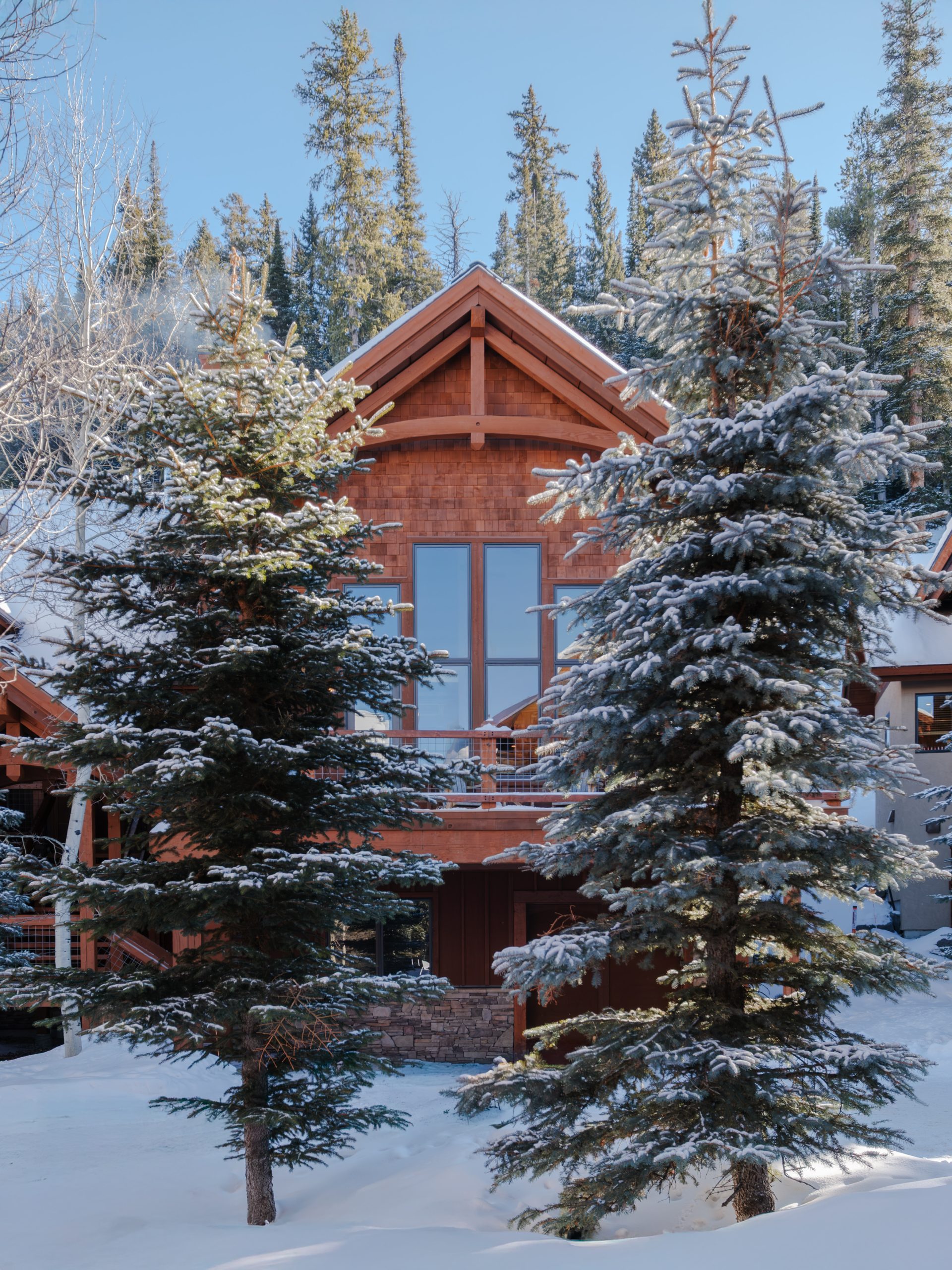 Front view of Big Sky mountain lodge with wood siding, balcony, and snowy evergreen landscape