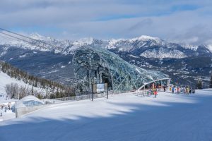 Big Sky Resort tram station with skiers, modern glass structure, and sweeping mountain views