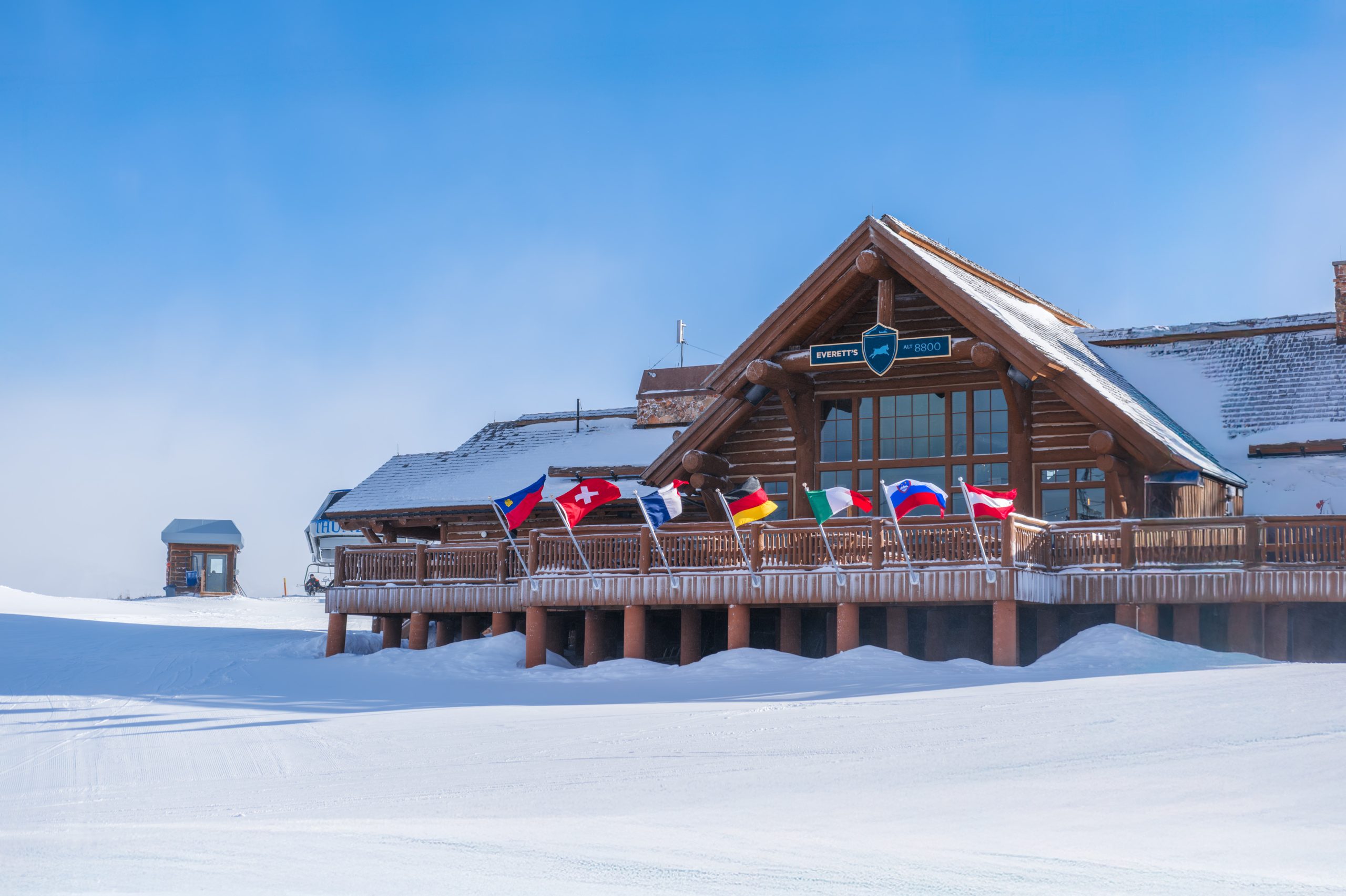 Everett’s 8800 summit lodge at Big Sky Resort with international flags and snowy alpine setting