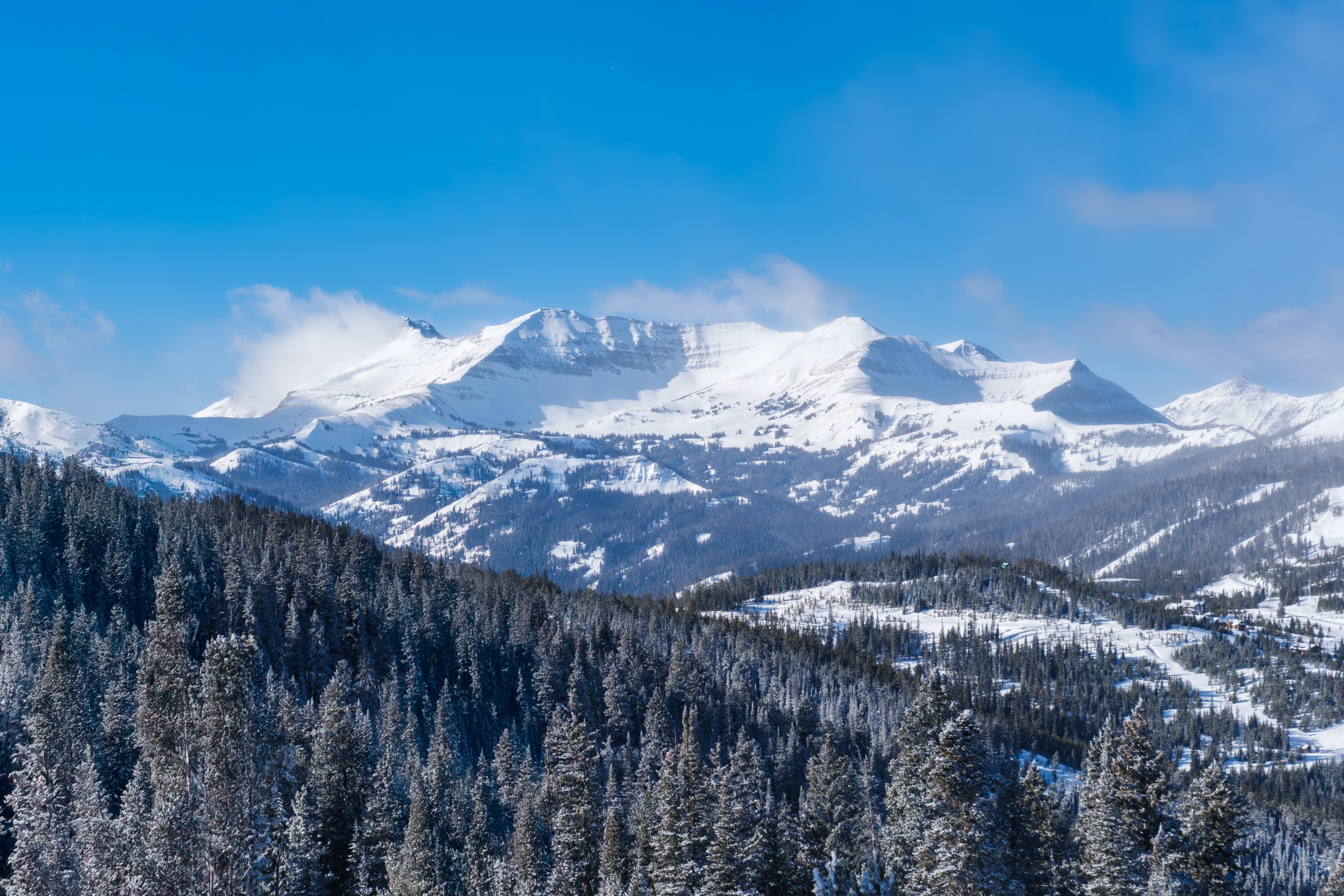 Wide panoramic view of Big Sky Resort mountains with snow-covered peaks and dense evergreen forest