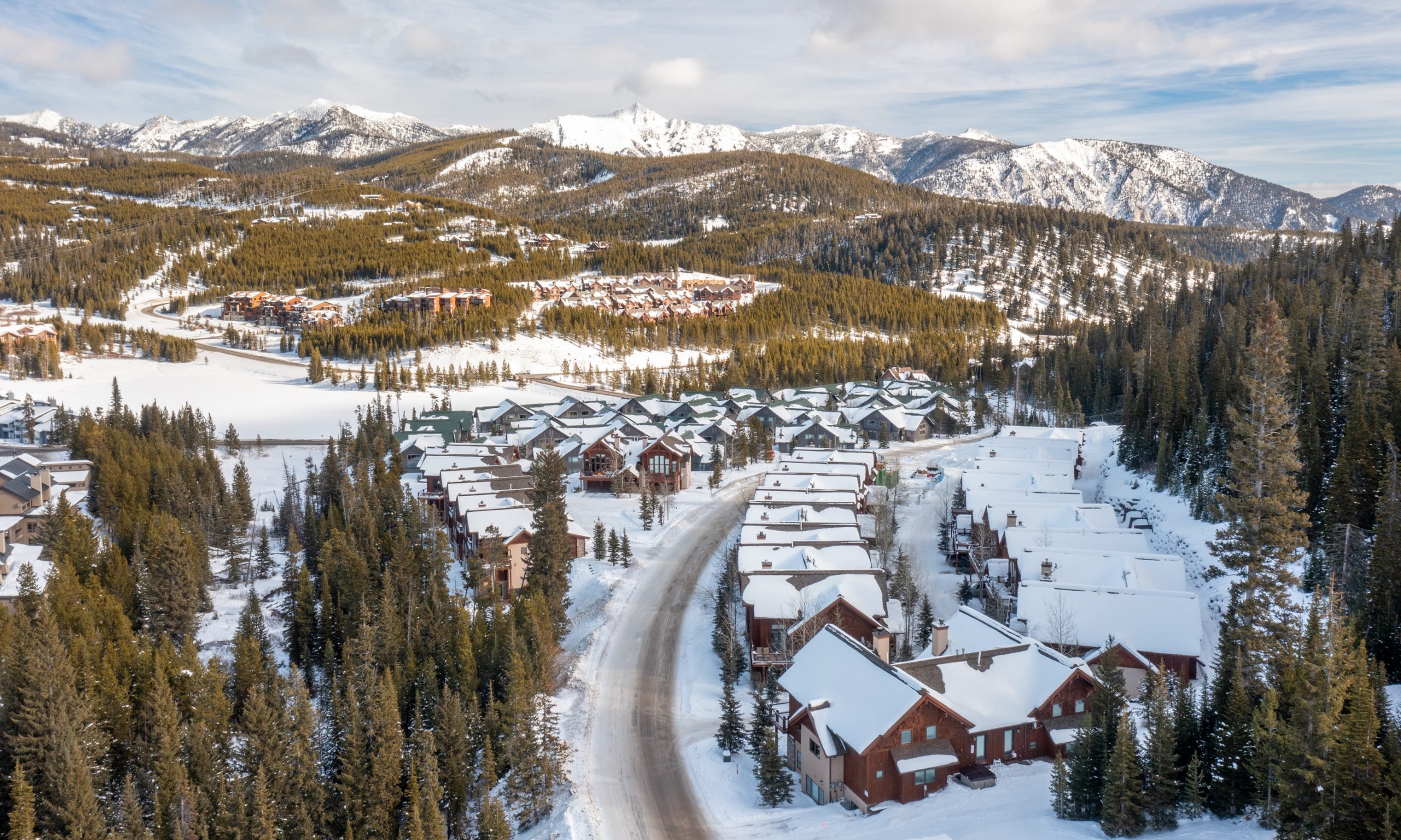 Scenic winter view of luxury ski-in/ski-out lodges in Big Sky Resort, surrounded by snow-covered mountains and pine trees.