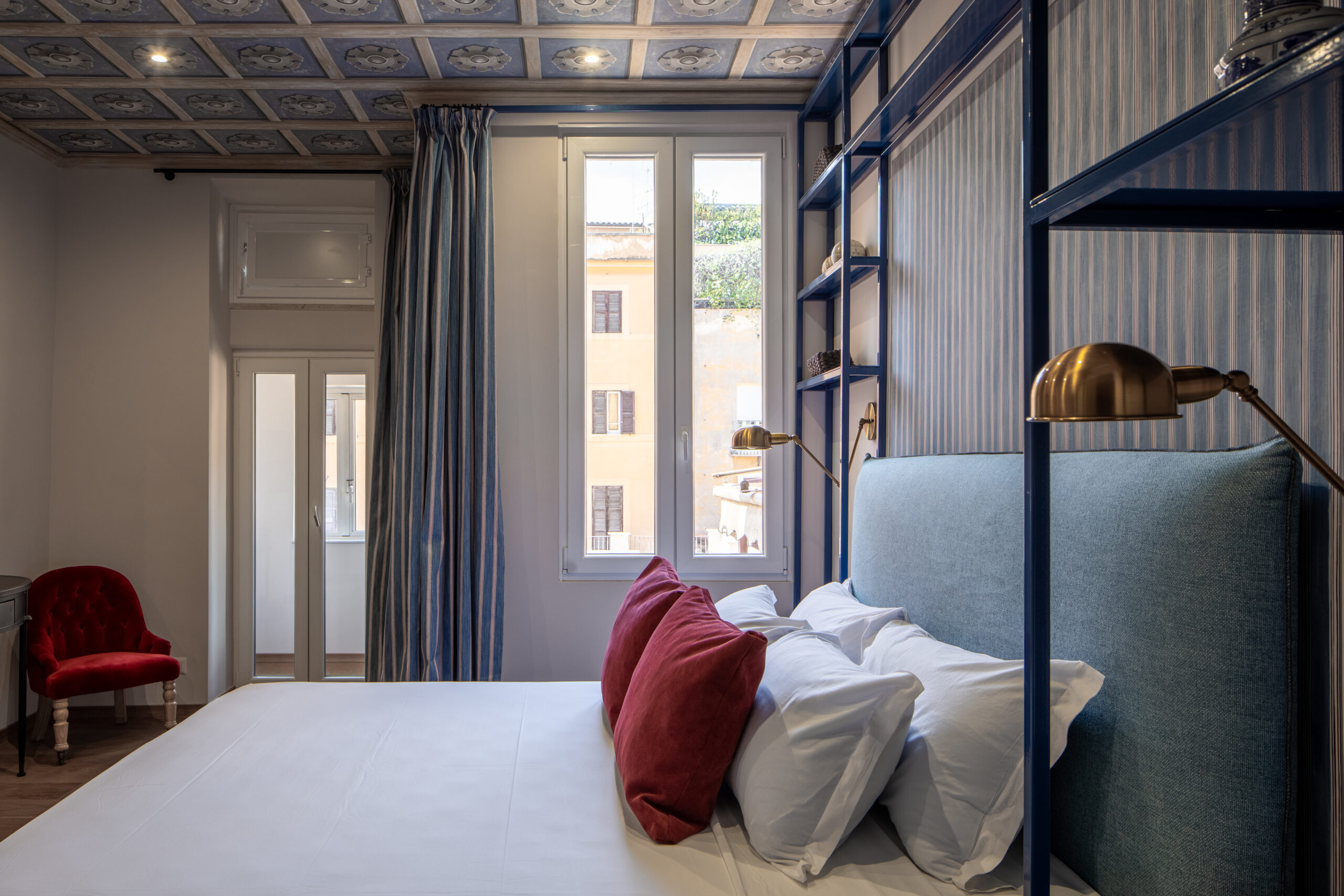 Elegant bedroom with an ornate ceiling, blue upholstered bed, and red accents in a Rome apartment by Equity Residences_