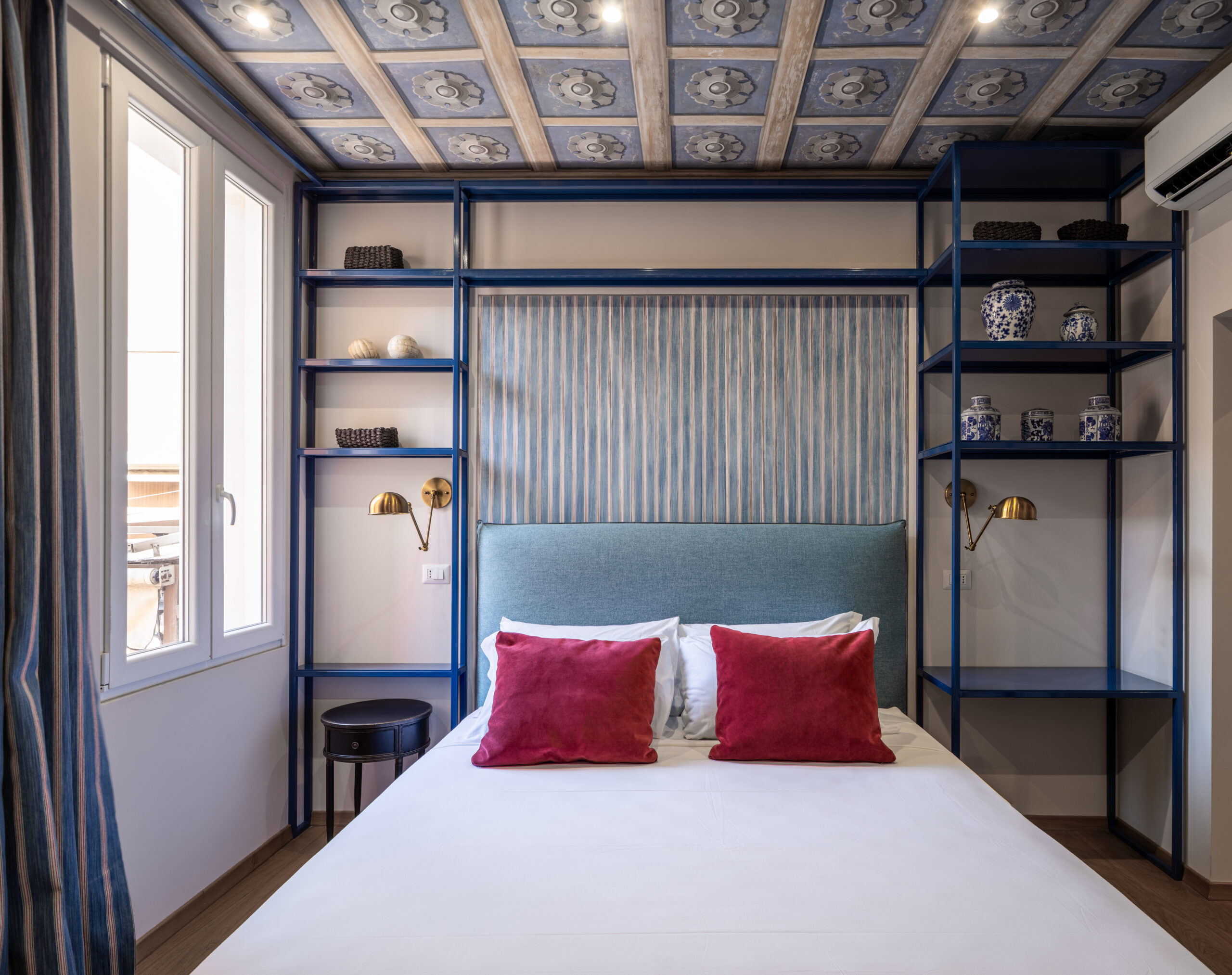 Elegant bedroom with an ornate ceiling, blue upholstered bed, and red accents in a Rome apartment by Equity Residences