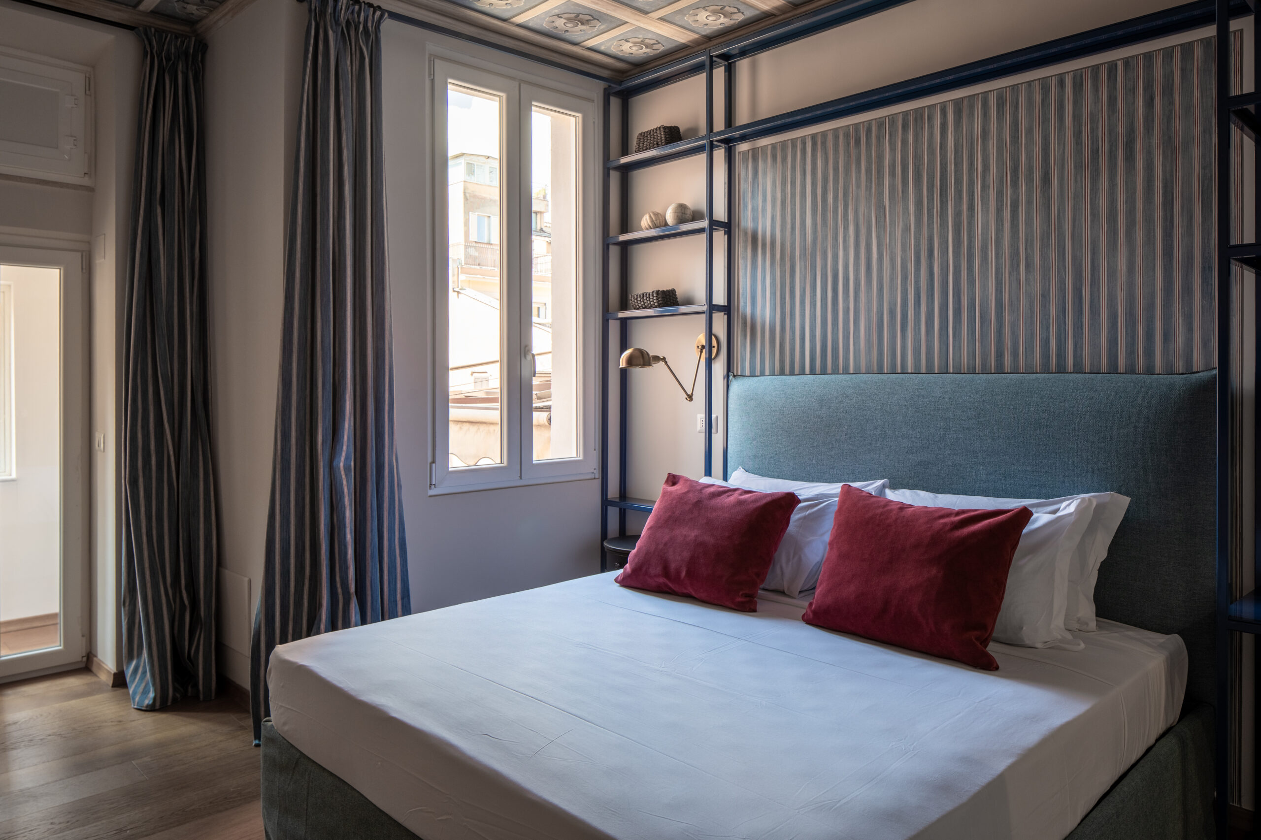 Elegant bedroom with an ornate ceiling, blue upholstered bed, and red accents in a Rome apartment by Equity Residences