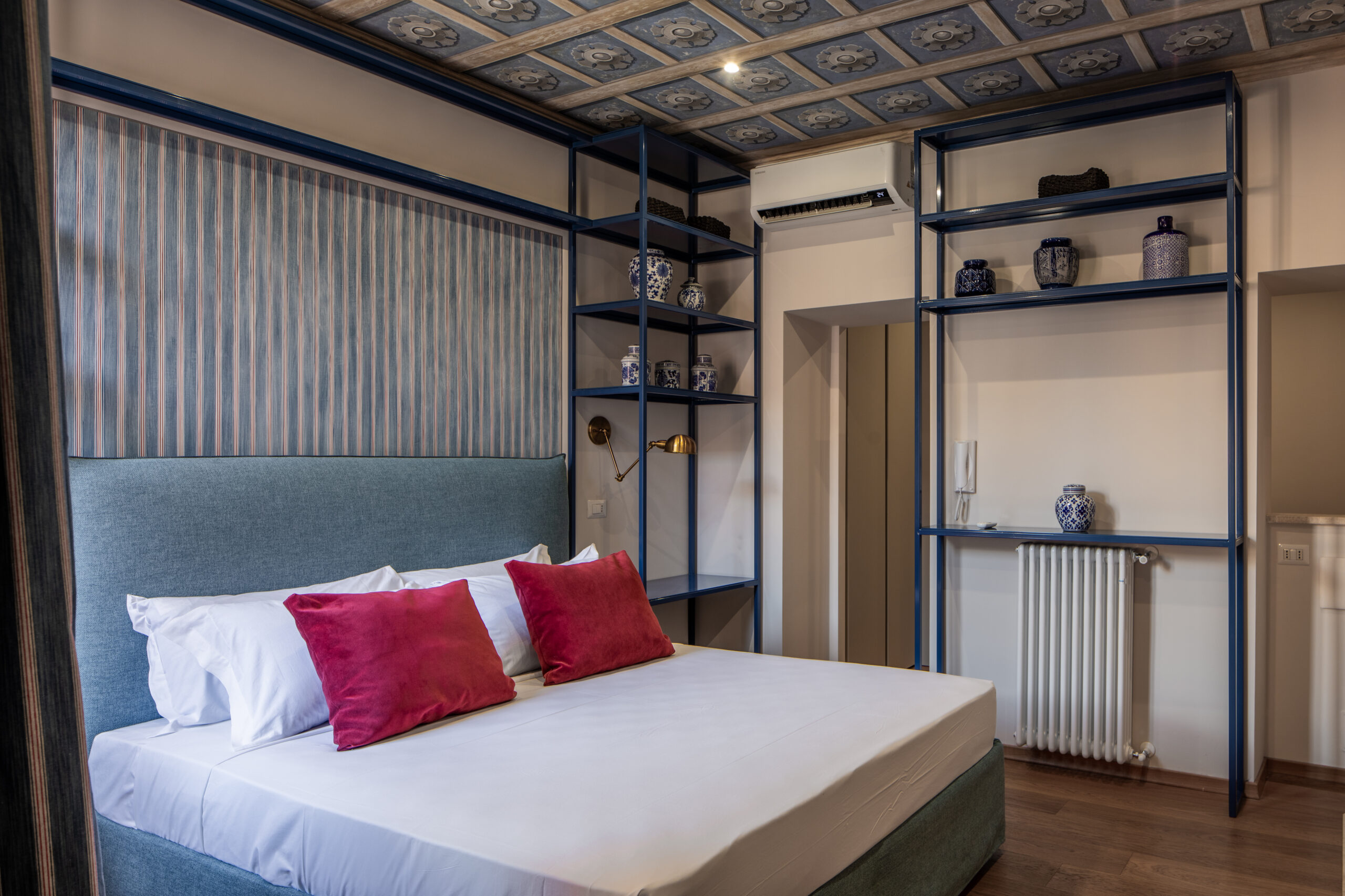 Elegant bedroom with an ornate ceiling, blue upholstered bed, and red accents in a Rome apartment by Equity Residences