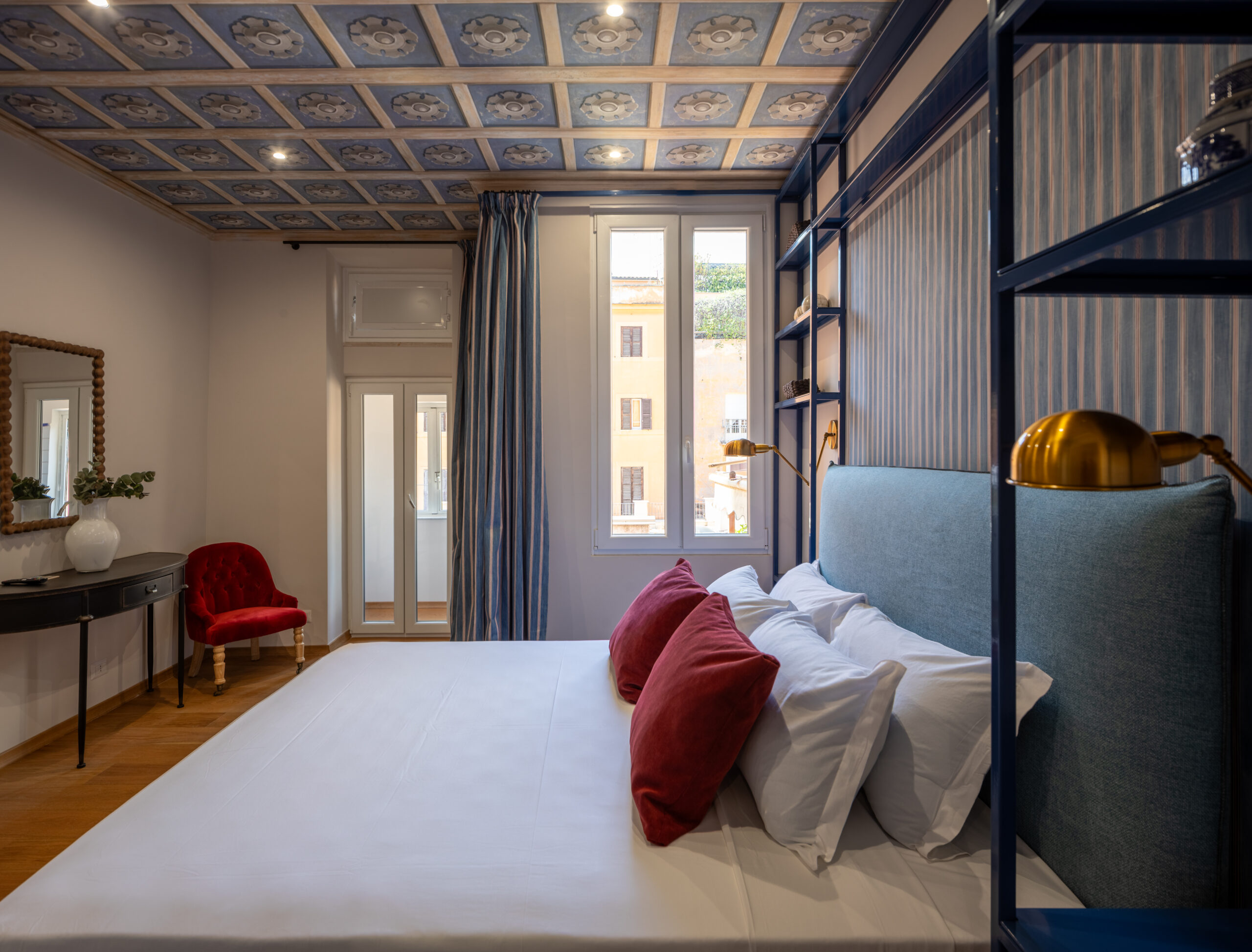 Elegant bedroom with an ornate ceiling, blue upholstered bed, and red accents in a Rome apartment by Equity Residences